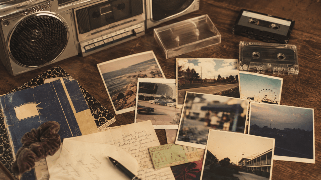 A nostalgic tabletop collage of late 1980s and early 1990s memories, including a boombox, cassette tapes, handwritten notes, old notebooks, and scattered printed photos on a wooden table.